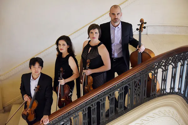 The four members of the Jupiter String Quartet stand on a staircase, dressed in formalwear, each holding their instrument (two violins, one viola, and a cello)