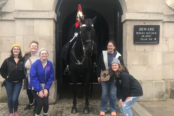Five students pose alongside a guard on horseback in London.